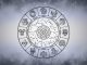 The Days Ahead Bring Heartache — Prepare Yourself Silver zodiac wheel with astrological symbols surrounded by soft gray mist on a bright celestial background